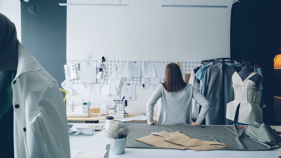 Fashion designer in studio surrounded by sewing patterns and garments.