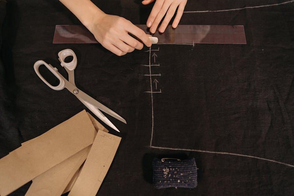 Close-up view of hands marking fabric for tailoring with scissors and ruler.